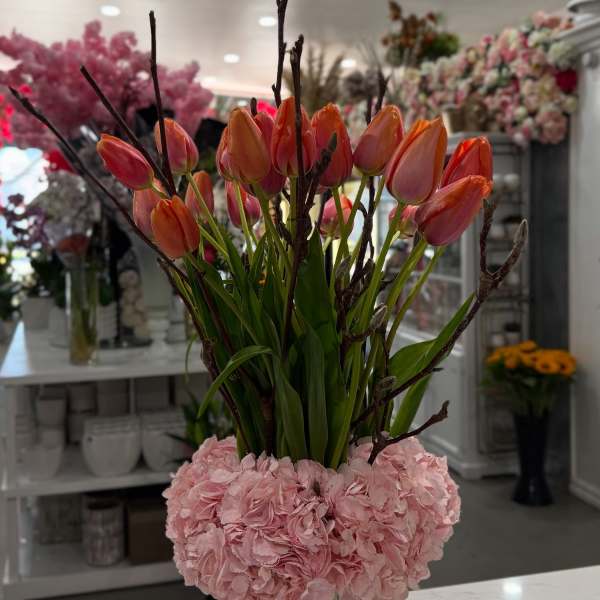 Pink hydrangeas with orange tulips in a clear square vase