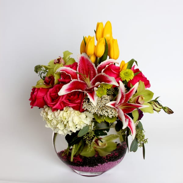 Mixed bouquet of pink roses, yellow tulips, and lilies in a glass vase