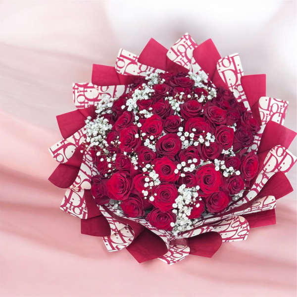 Large bouquet of deep red roses with white filler blooms wrapped in red and patterned paper