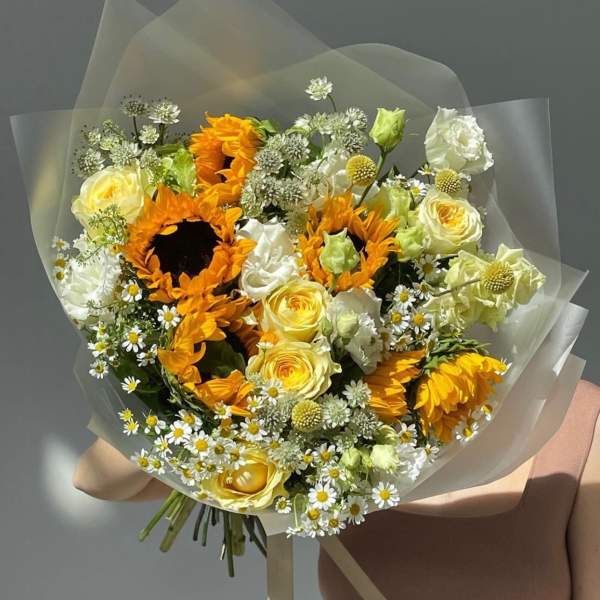Bouquet of sunflowers, yellow roses, and white daisies wrapped in clear paper