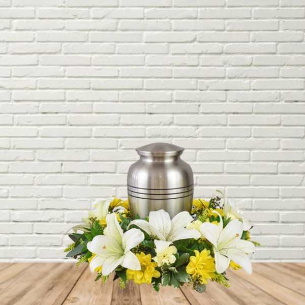 White lilies and yellow flowers arranged around a silver urn