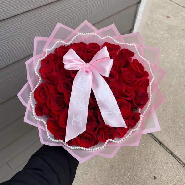 Round bouquet of red roses wrapped in pink paper with a satin bow