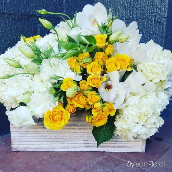 White hydrangeas and yellow roses arranged in a wooden box