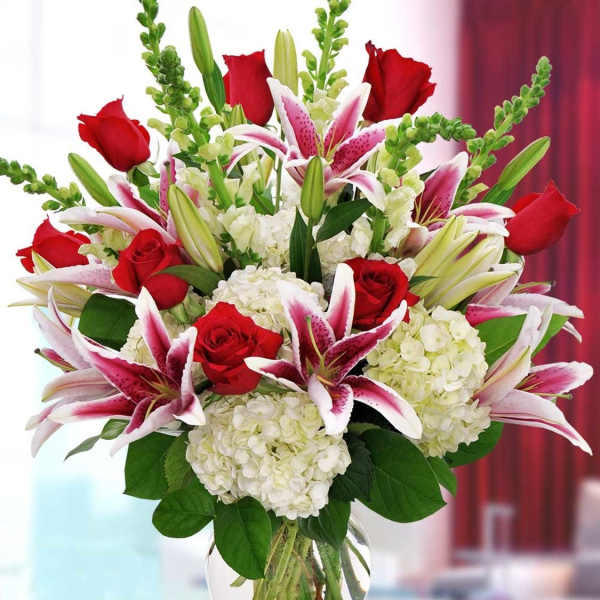 Bouquet of red roses, pink lilies, and white hydrangeas in a glass vase
