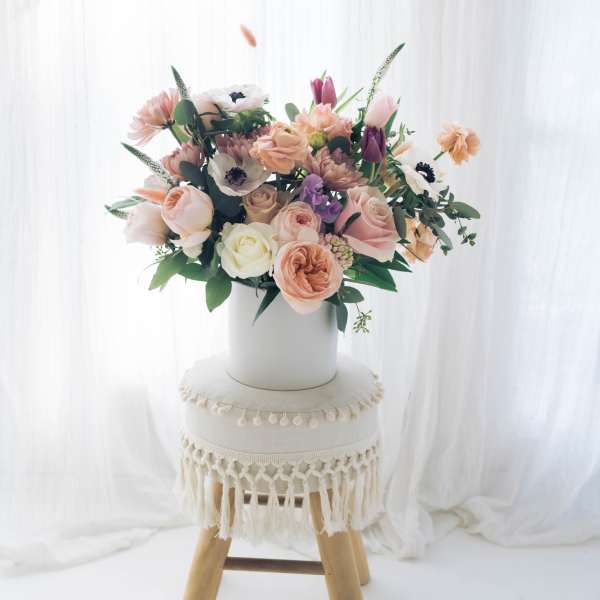 Pastel flower arrangement in a white vase on a stool