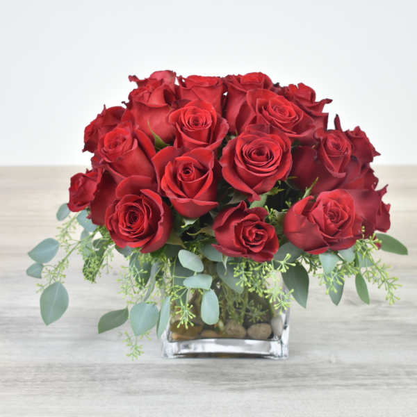Low arrangement of red roses in a clear glass cube vase with trailing greenery