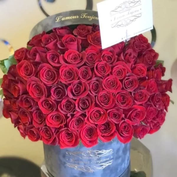 Round box filled with tightly packed red roses and a small card on top