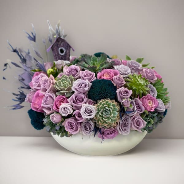 Lavender roses and succulents arranged in a white bowl vase