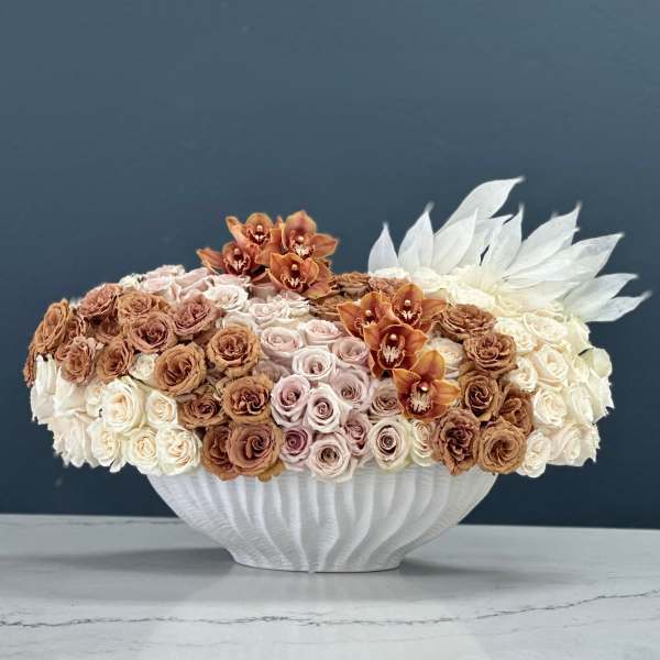 Low floral arrangement of roses and orchids in a white vase