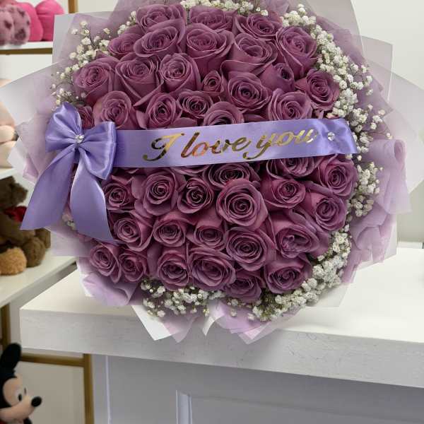Bouquet of purple roses with a lavender ribbon and white filler flowers