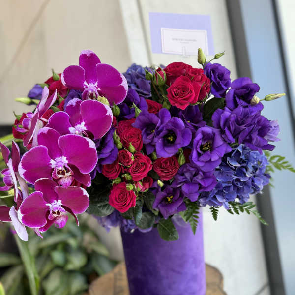 Purple and pink bouquet with orchids, roses, and hydrangeas in a purple vase