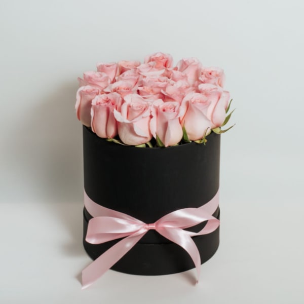 Pink roses arranged in a black round box with a pink ribbon