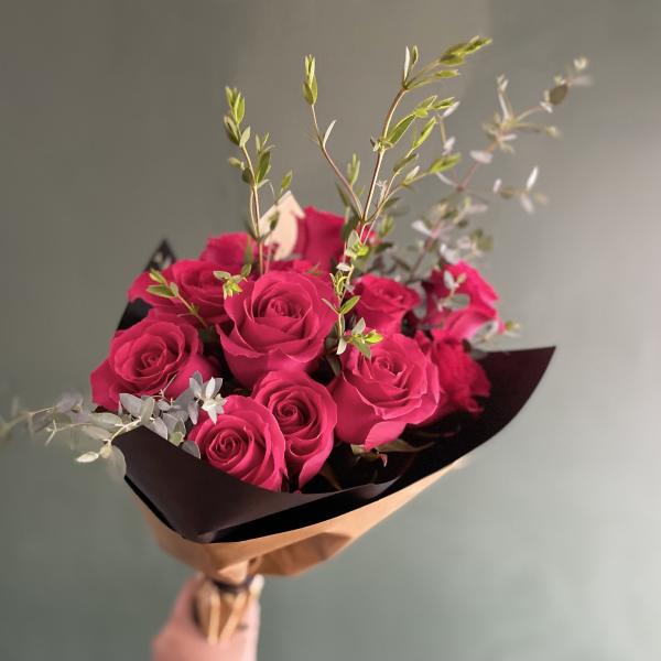 Bouquet of bright pink roses with airy greenery in dark wrap