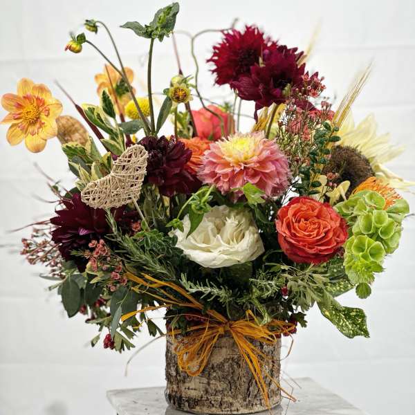 Mixed bouquet in a bark-covered container with burgundy, peach, white, and green flowers