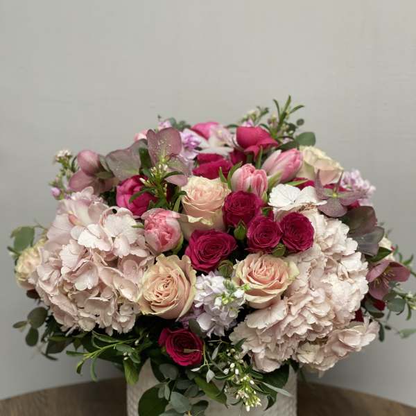 Low round arrangement of pink hydrangeas, roses, and tulips in a white ceramic vase