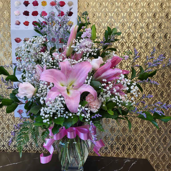 Pink lilies and roses in a glass vase with a pink ribbon