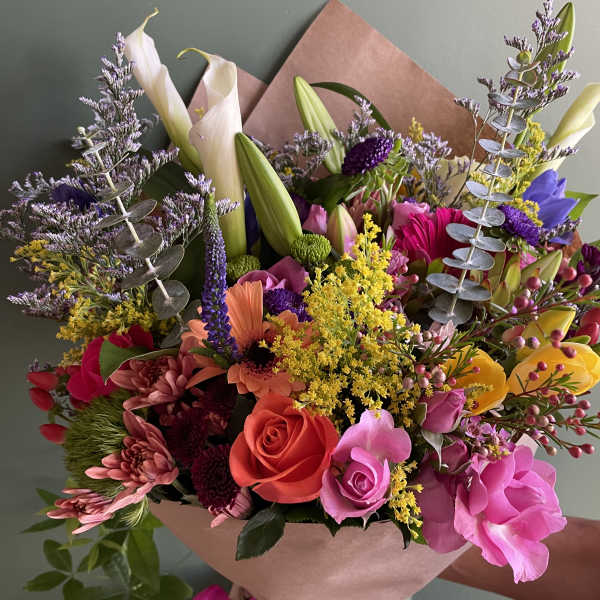 Colorful bouquet with roses, lilies, and mixed blooms wrapped in pink paper