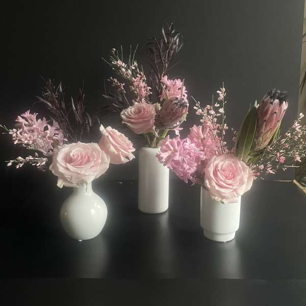 Three small pink floral arrangements in white vases on a dark surface