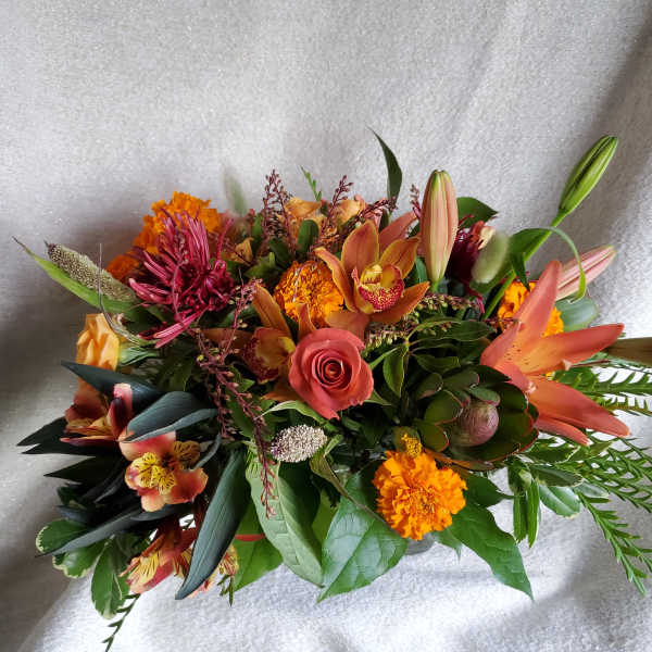 Low arrangement of orange lilies, roses, marigolds, orchids and mixed blooms in warm autumn tones