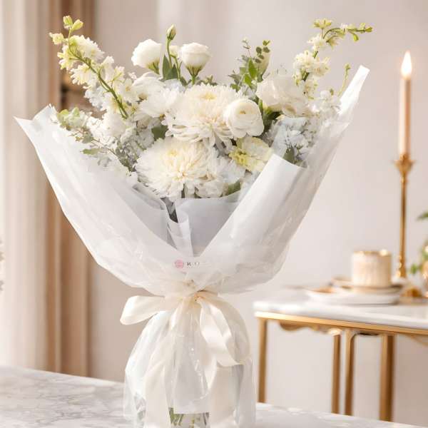 White bouquet of mixed flowers wrapped in sheer paper with a ribbon