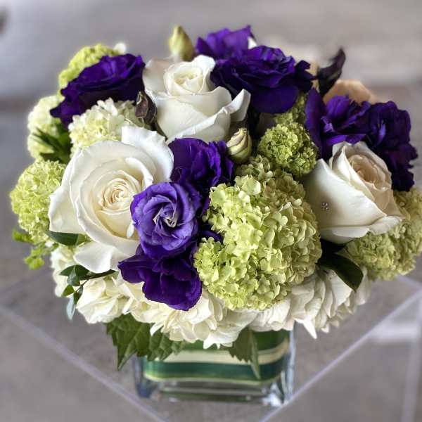Bouquet of white roses, purple lisianthus, and green hydrangeas in a glass vase