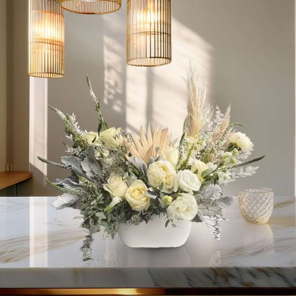 White floral arrangement in a low ceramic vase with dried grasses