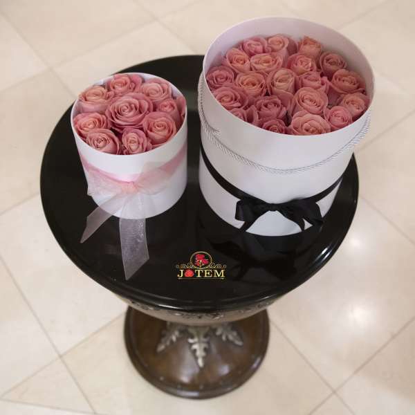 Two round boxes filled with pink roses and ribbon bows