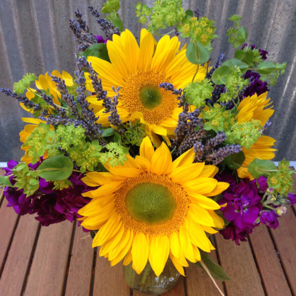 Bright sunflower arrangement with purple flowers in a clear glass vase on a wooden table