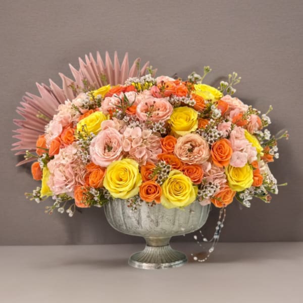 Mixed pink, orange, and yellow roses in a silver pedestal vase