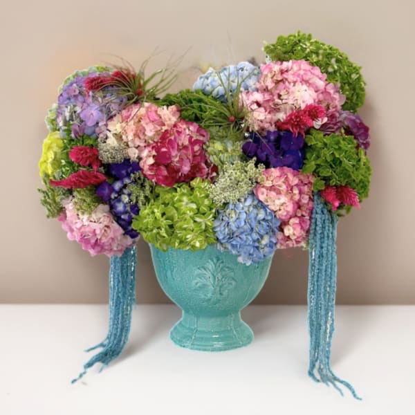 Colorful hydrangea arrangement in a turquoise vase with hanging blue strands