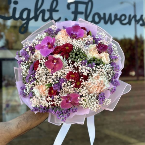 Large bouquet of pink orchids, red blooms, and purple filler flowers wrapped in pastel paper