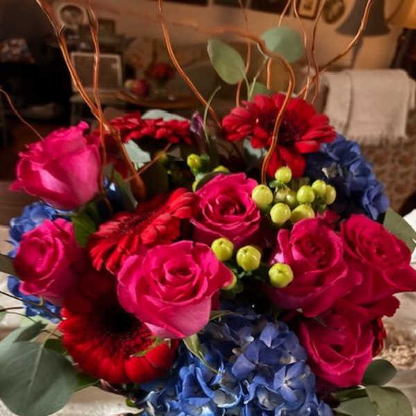 Bouquet of pink roses, red gerberas, and blue hydrangeas in a glass vase