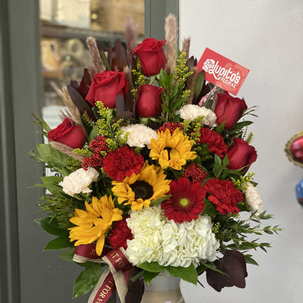 Mixed bouquet of red roses, yellow sunflowers, and white hydrangea in a decorative vase
