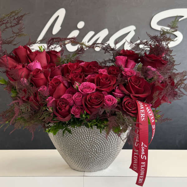 Red and pink roses arranged in a silver textured vase with a ribbon