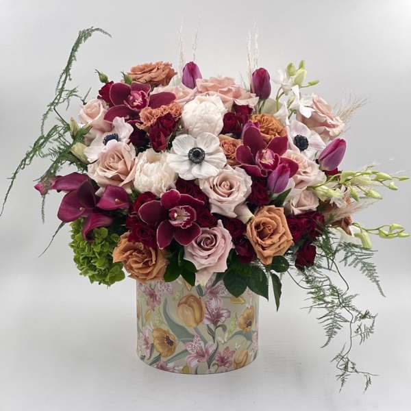 Mixed bouquet of roses, orchids, and tulips in a floral-patterned box