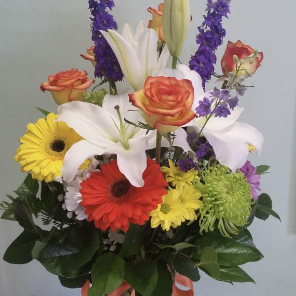 Mixed bouquet with roses, lilies, gerbera daisies, and purple spikes in a glass vase