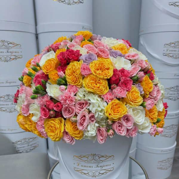 Round bouquet of pink, yellow, white, and lavender roses in a white hat box