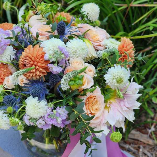 Mixed bouquet of peach, white, lavender, and blue flowers with ribbon tails