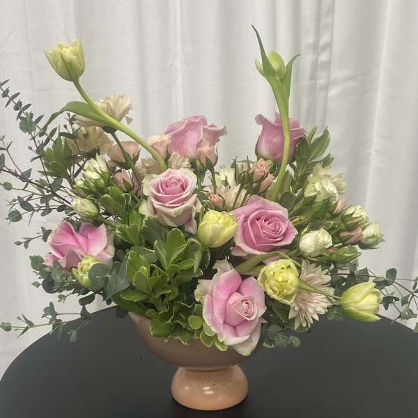 Pink roses and pale blooms arranged in a pedestal bowl vase