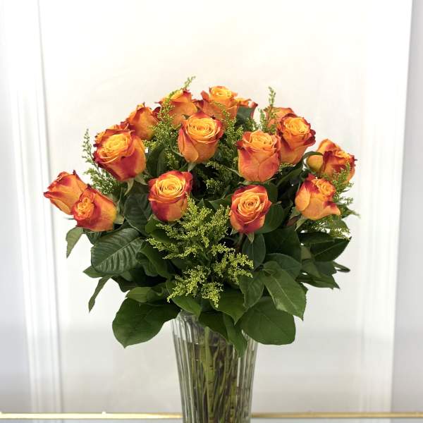 Orange roses arranged in a tall clear glass vase