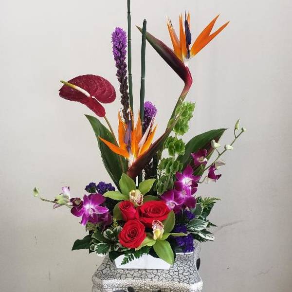 Tropical flower arrangement with red roses and purple orchids in a decorative vase