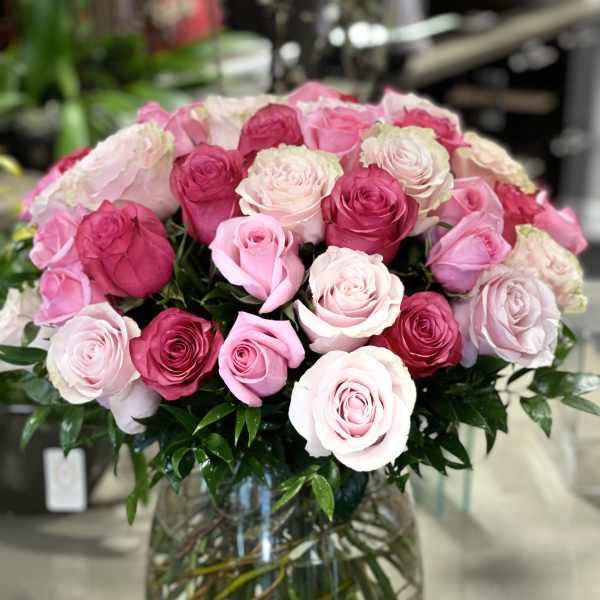 Large bouquet of pink roses in varying shades arranged in a round clear glass vase.