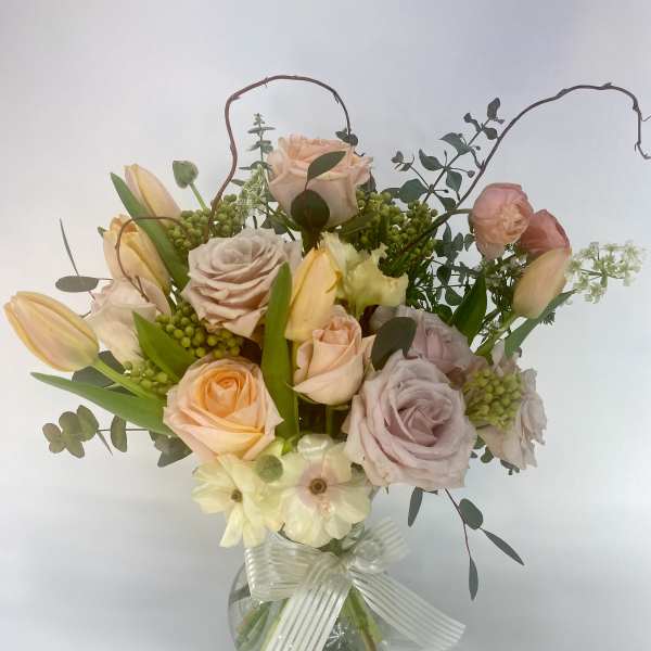 Mixed pastel roses and tulips in a clear glass vase with a ribbon