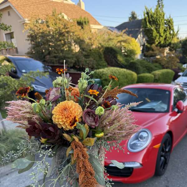 Handheld bouquet with orange, burgundy, and pink flowers