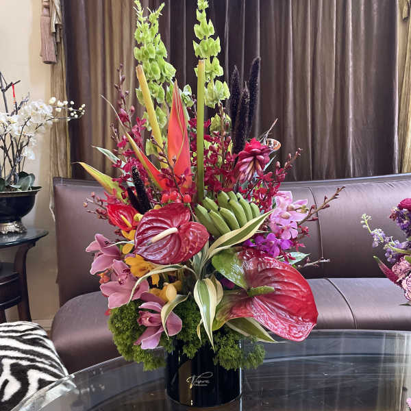 Tall tropical flower arrangement in a black vase with red anthuriums and pink orchids