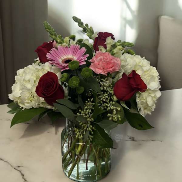 Bouquet of red roses, pink gerbera daisy, and white hydrangeas in a glass vase