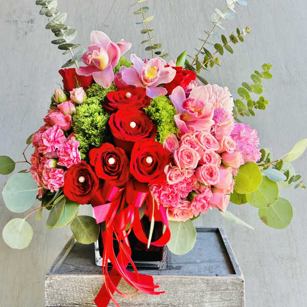 Red and pink floral arrangement in a black vase with ribbon