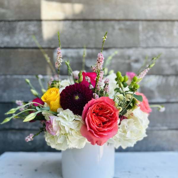Mixed bouquet of roses, hydrangeas, and other blooms in a white vase