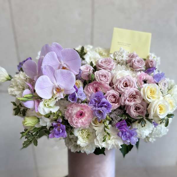 Lavender orchids and pink roses arranged in a pink vase