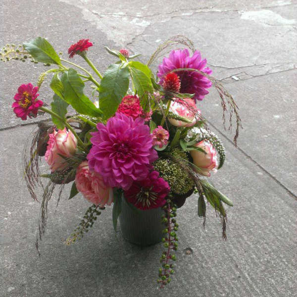 Vase arrangement of bright pink dahlias and blush roses with mixed accents on a concrete surface